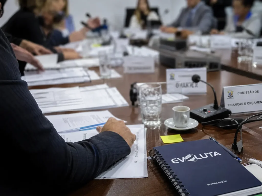 Plenário vazio de câmara municipal com caderno da Evoluta, tema da reforma administrativa do Legislativo